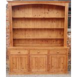 A waxed pine dresser with plate shelves over three drawers and cupboards, on block base