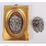 A pair of cast iron lions' heads, one in gilt frame