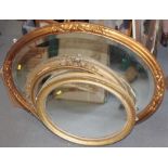 An oval gilt framed wall mirror with bevelled glass, plate 23" x 30 1/2", and two other similar