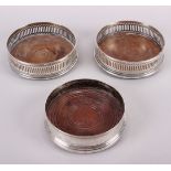 A pair of silver bottle coasters with pierced galleries and turned wooden bases and one other silver
