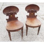 A pair of George III carved mahogany hall chairs with shell backs and panel seats, on turned
