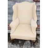 A wing armchair of Georgian design, upholstered in a natural fabric, on cabriole supports and pad