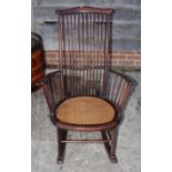 A tall spindle back rocking chair with caned seat panel