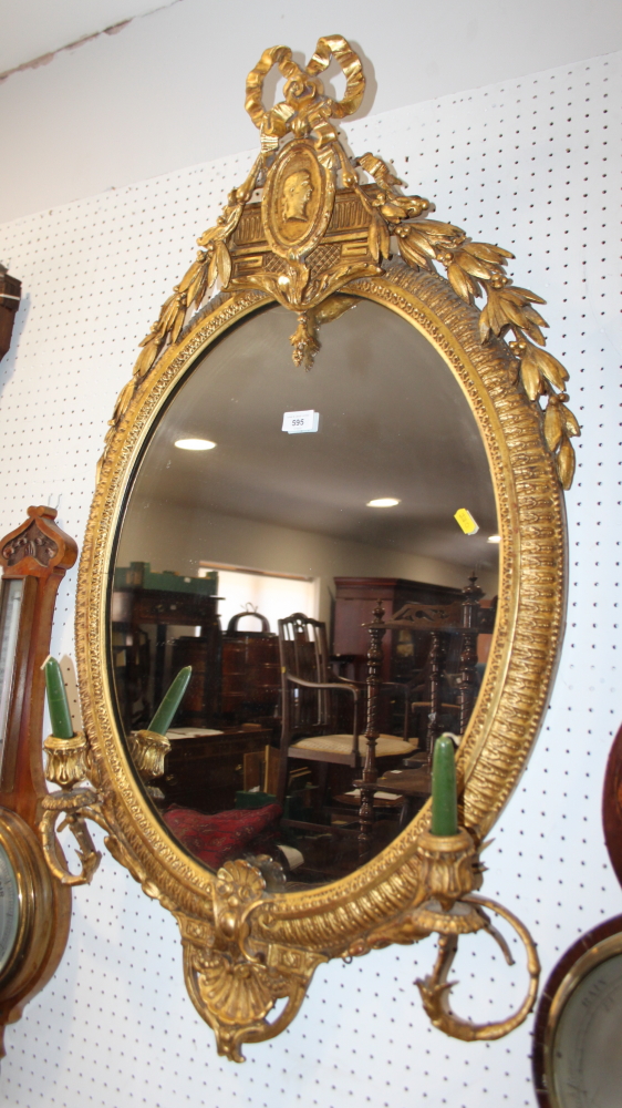 A 19th century oval gilt framed girandole with ornate ribbon and husk surmount, fitted two
