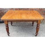 An Edwardian walnut extending dining table with one extra leaf, on turned tapering castored supports