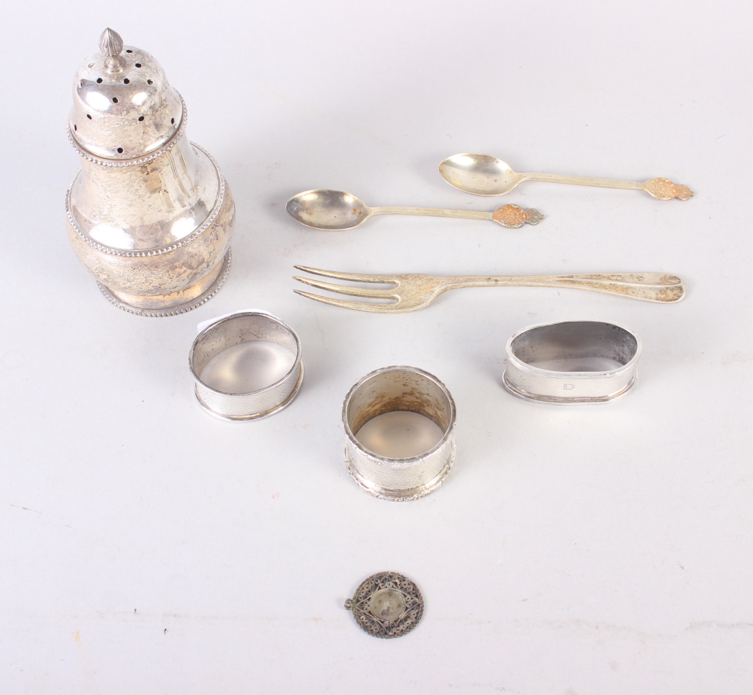 A silver sugar caster, three silver napkin rings, a silver fork, two silver teaspoons and a white