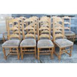 A set of fourteen oak ladder back chairs with shaped top rails and padded seats
