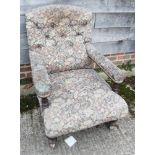 A button back low armchair, upholstered in a floral fabric, on turned and castored supports