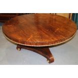 A Regency rosewood circular tilt top dining table with gilt moulding to freeze, on fluted column and