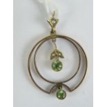 An Edwardian 9ct gold peridot and seed pearl pendant having floral drop within geometric circular