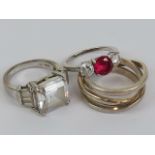 Three silver rings; one with central red stone flanked by twin round cut white stones size N-O,