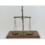 A vintage set of brass balance scales raised over mahogany plinth,