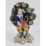 An early 19th Century seated Derby figurine in floral surround standing 13cm high.