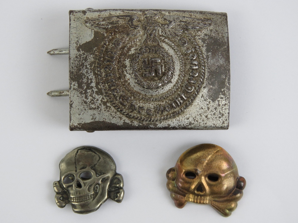 A WWII German SS belt buckle together with two SS Totenkopf skull cap badges.