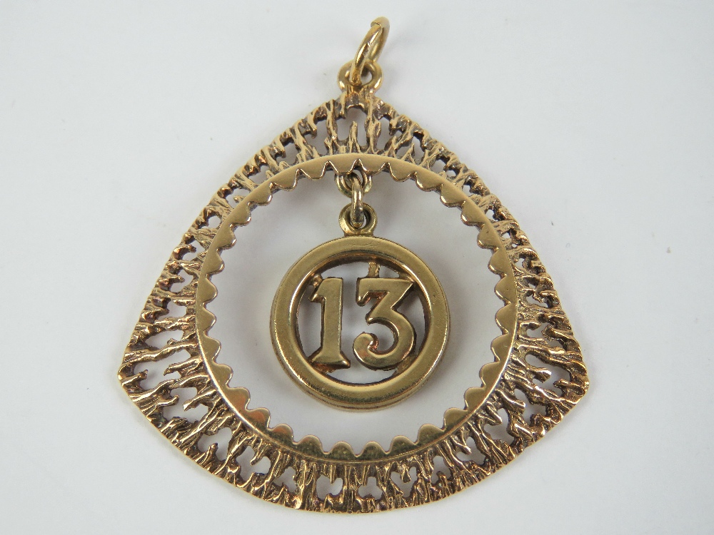 A 9ct gold '13' charm suspended within triangular bark effect pendant,