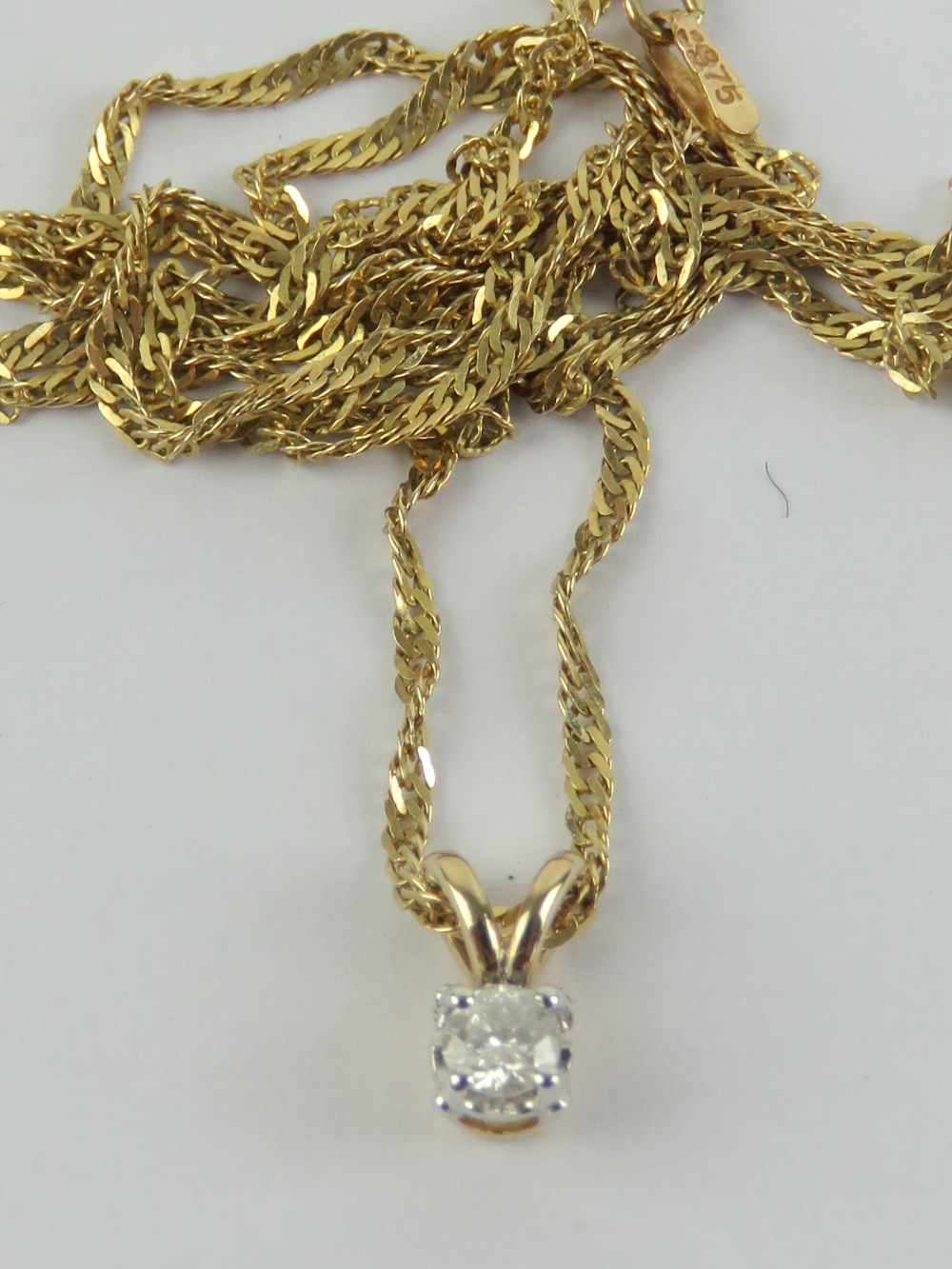 A solitaire diamond pendant, claw set in white white metal on yellow metal, measuring 0.