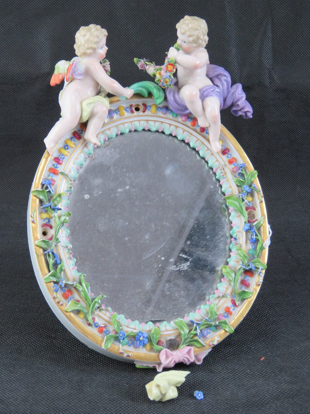 A late 19th century Continental floral encrusted oval easel mirror decorated with cherubs upon,
