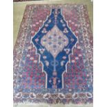 A vintage hand knotted rug in reds and blues having geometric decoration and measuring 196 x 135cm.