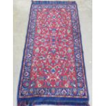 A woollen and silk rug in reds and blues having floral decoration upon 135 x 65cm.