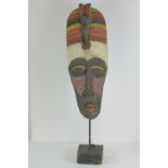 A carved and painted wooden African mask on stand, 80cm high.