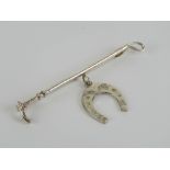 A silver stock pin or brooch in the form of a riding crop with horse shoe under, marked sil,