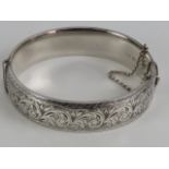 A HM silver hinged bangle having floral engraved decoration to front, with safety chain,