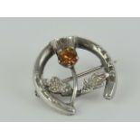 A sterling silver stock pin or brooch having horseshoe and thistle with orange stone upon,
