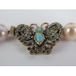A string of peach coloured pearls having silver butterfly clasp set with turquoise and white stones,