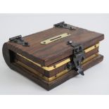 A wooden money box in the form of a book, having brass escutcheon and black metal hinges. 18 x 15cm.