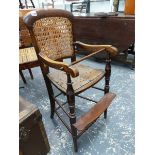 A STAINED WOOD CHILD'S CANED BACK HIGH CHAIR, THE PIERCED SEAT ABOVE A FOOT REST JOINING THE