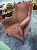 AN EDWARDIAN FIRESIDE ARMCHAIR ON SQUARE TAPERED LEGS WITH BRASS CASTERS.