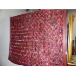 AN INDIAN PATCHWORK PANEL WORKED WITH RED SILK GEOMETRIC SHAPES WITHIN A FLORAL BORDER AND BACKED BY