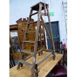 A SLINGSBY PINE LADDER SLOPING TO A RIGHT ANGLE SUPPORT WITH IRON WHEELS AT THE BASE SPRUNG SO