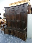 AN 18th.C.AND LATER OAK CURVED BACON SETTLE WITH PANEL DOORS OVER SHAPED SEAT AND FOUR DEEP BASE