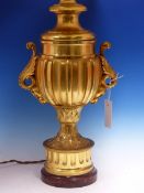 A GILT BRONZE LAMP BASE OF FLUTED BALUSTER SHAPE WITH FOLIATE HANDLES THE CIRCULAR FOOT ON RED