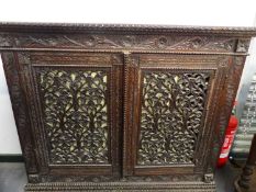 A COLONIAL HARDWOOD SIDE CABINET WITH CARVED DECORATION, A PAIR OF PIERCED PANEL DOORS ENCLOSING A