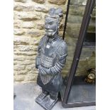 A CHINESE BLACKENED TERRACOTTA SOLDIER STANDING WITH HIS HANDS CLASPED ON HIS LACQUER ARMOURED