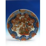 AN ANTIQUE JAPANESE IMARI DISH, THE CENTRAL VASE OF FLOWERS BELOW TASSELLED KNOTS WITHIN A BLUE