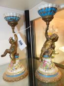 A PAIR OF PORCELAIN AND BRASS CHERUBIC CANDLESTICKS.