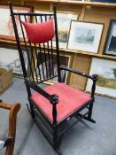 AN EBONISED WOOD ROCKING CHAIR. RED SEAT, DISC KNOPPED HAND RESTS TO THE STRAP ARMS.