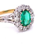 AN EMERALD AND DIAMOND CLUSTER RING. THE PRINCIPLE MIXED CUT EMERALD IN A TWELVE CLAW SETTING