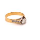 AN 18ct GOLD AND DIAMOND SOLITAIRE RING, WITH GRAIN SET DIAMOND CHANNEL SHOULDERS. APPROX