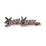 AN ANTIQUE DIAMOND PAVE SET BROOCH DEPICTING A PAIR OF RUNNING HARES WITH GEM SET EYES.