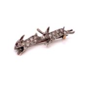 AN ANTIQUE DIAMOND PAVE SET BROOCH DEPICTING A PAIR OF RUNNING HARES WITH GEM SET EYES.