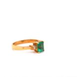 AN 18k YELLOW GOLD EMERALD AND DIAMOND RING. THE CENTRAL EMERALD FLANKED BY A SINGLE BRILLIANT CUT