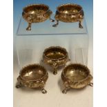 A SET OF FIVE VICTORIAN HALLMARKED SILVER REPOUSSE DECORATED TABLE SALTS ON HOOF FEET TOGETHER