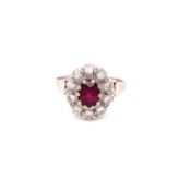 AN 18ct WHITE GOLD RUBY AND DIAMOND CLUSTER RING. THE OVAL CLAW SET RUBY SURROUNDED BY A CLUSTER