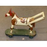 A PAINTED WOOD SKEWBALD PUSH ALONG HORSE ON GREEN PLINTH AND WHEELS. H 44.5cms.