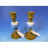 A PAIR OF GILT METAL CANDLESTICKS WITH OVOID PORCELAIN KNOPS CENTRAL TO THE COLUMNS AND DECORATED IN