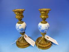 A PAIR OF GILT METAL CANDLESTICKS WITH OVOID PORCELAIN KNOPS CENTRAL TO THE COLUMNS AND DECORATED IN